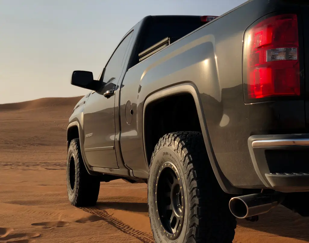 Rear side view of a pickup truck parked on desert sand.