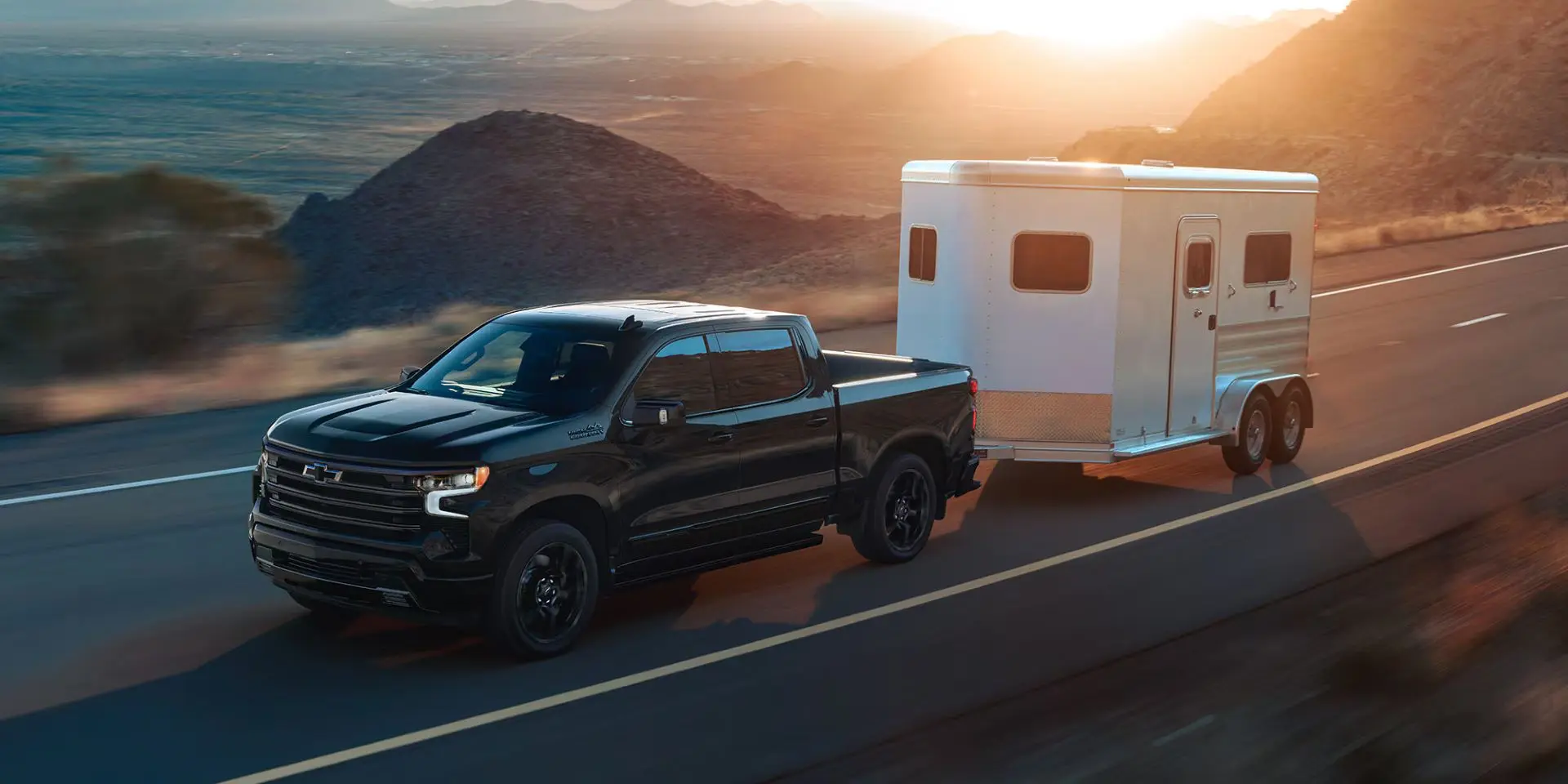 a 2025 chevrolet silverado 1500 driving on a paved road hauling a horse trailer