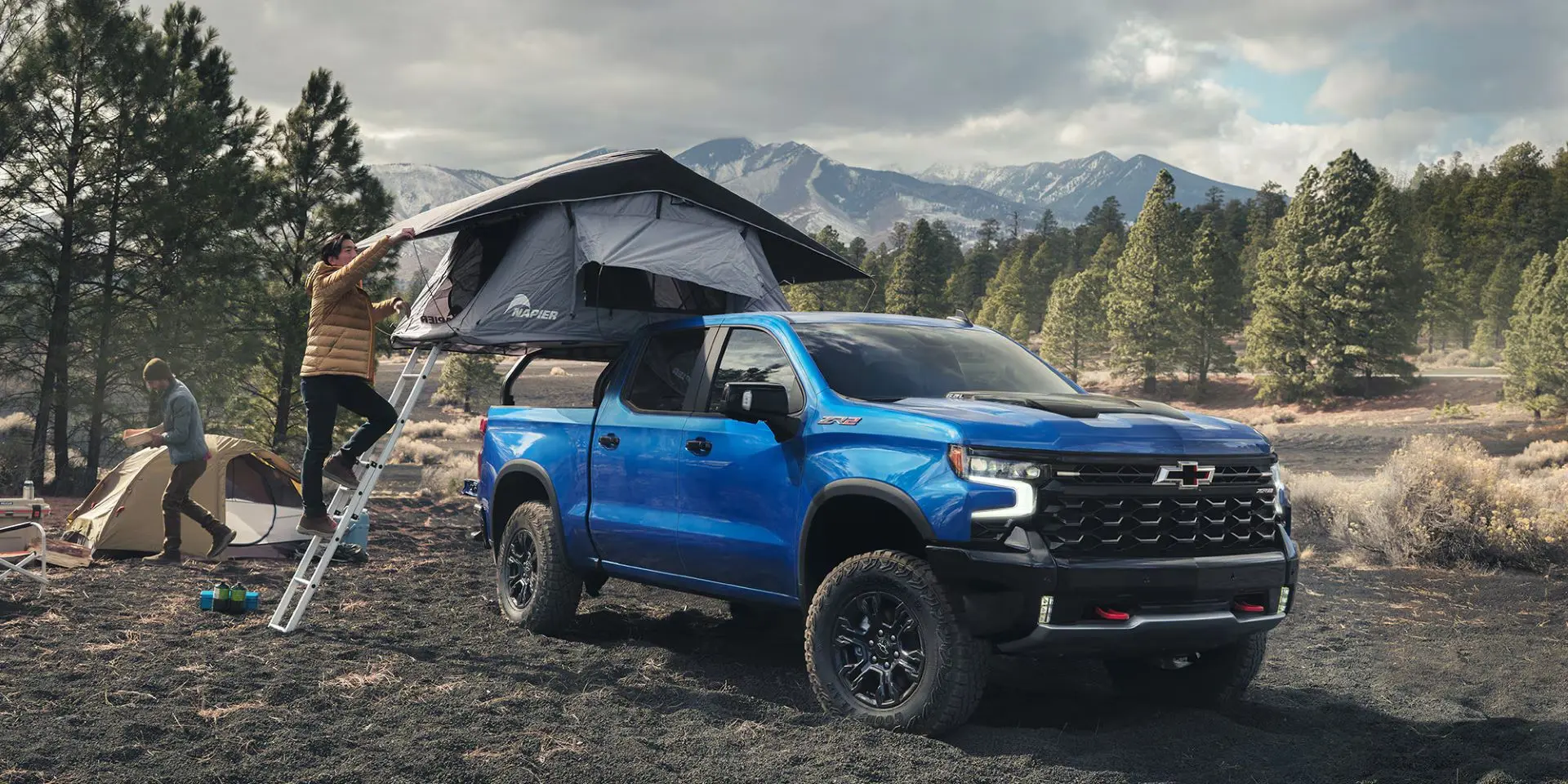 2025 chevy silverado parked in the woods with a pop up camper in the bed