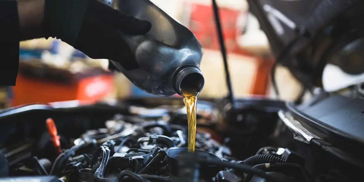 Technician pouring motor oil into a vehicle engine during an oil change