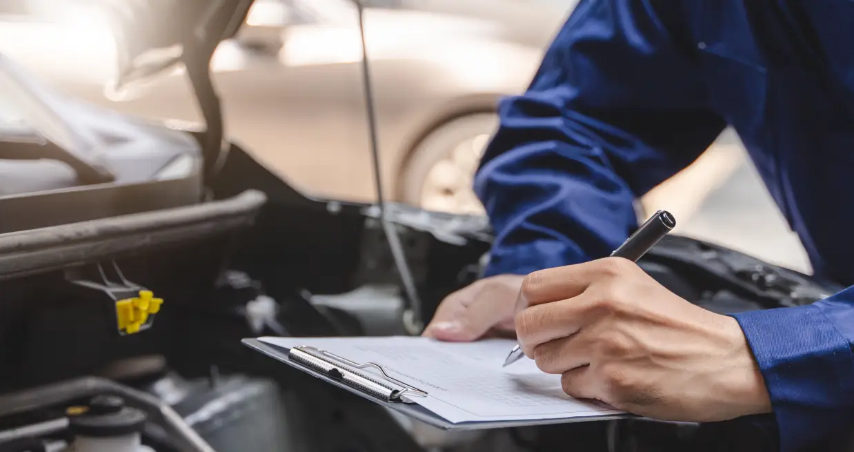 Technician inspecting a vehicle and taking notes beside the open hood