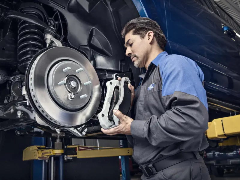Ford technician installing a brake caliper over a brake rotor on a vehicle lift