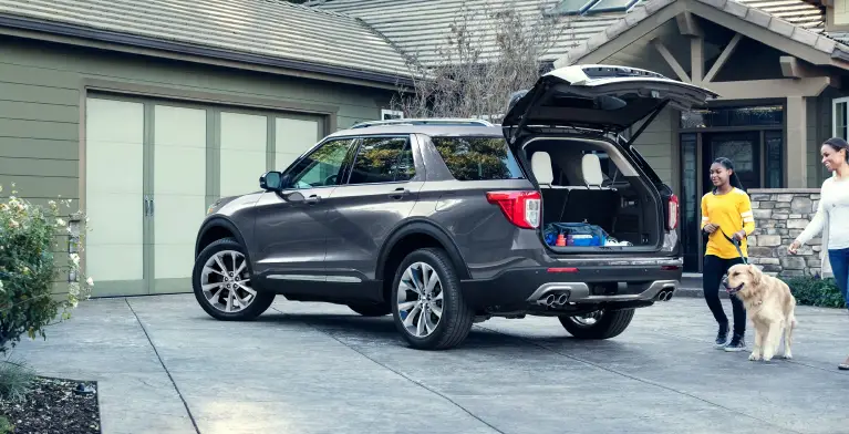 Family with a dog walking up to a Ford Explorer with its rear liftgate open in a driveway