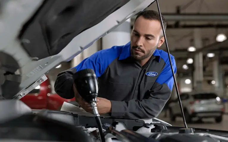 Ford technician using a tool under the hood during routine maintenance