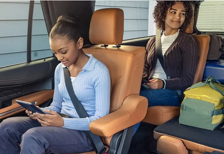 Two smiling children using mobile devices in the second and third rows of a Ford SUV