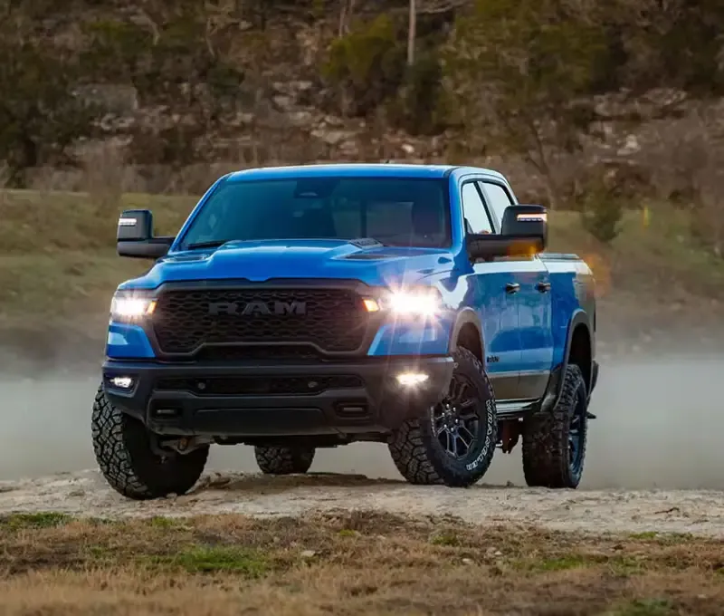 Blue Ram 1500 driving on a dusty trail with LED headlights on
