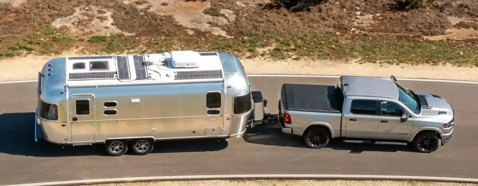 Ram 1500 towing a silver travel trailer on a desert road