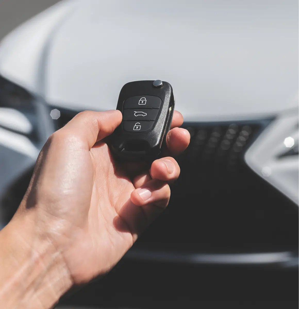 Close-up of a person holding a car key remote near a vehicle.