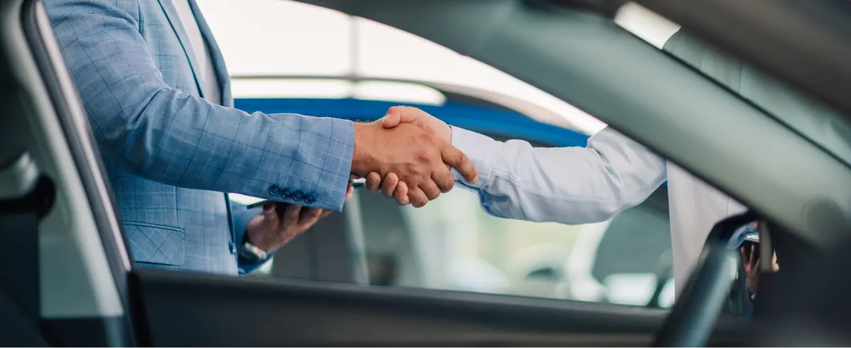 Customer shaking hands with a salesperson through the window of a car after financing a vehicle at Mathis Motors in St. Charles, MO