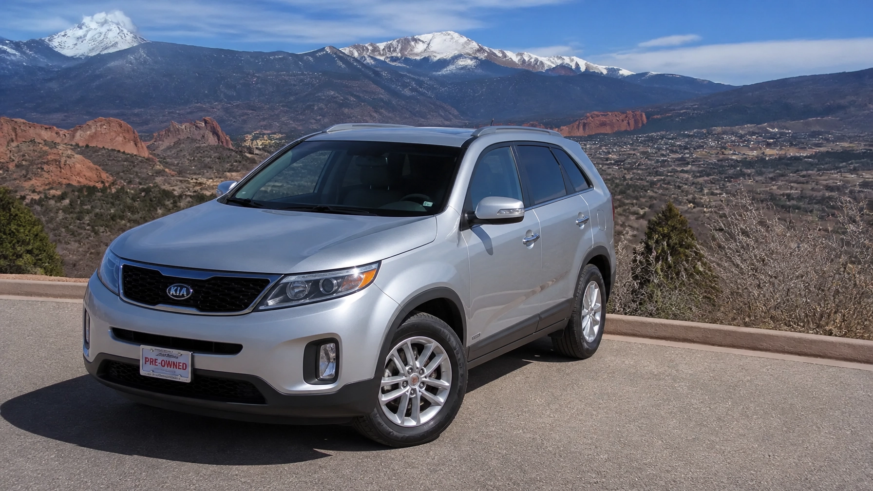 A professional photograph of a modern pre-owned silver SUV at a scenic Colorado Springs overlook with Pikes Peak in the background