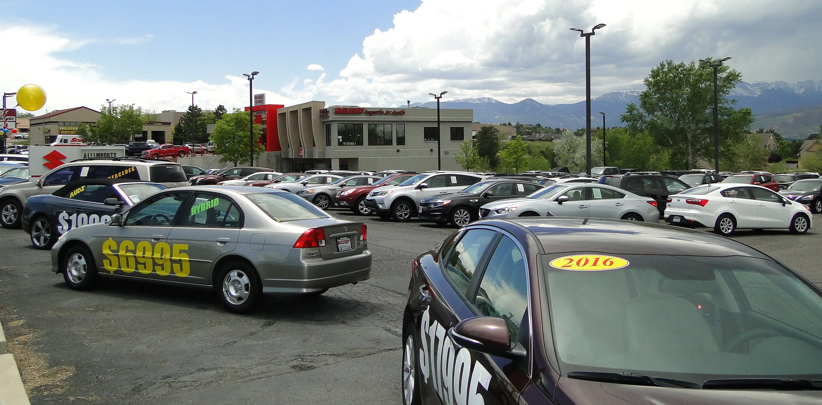 A large selection of pre-owned cars and SUVs at the McCloskey Motors lot with a scenic mountain view in the background.