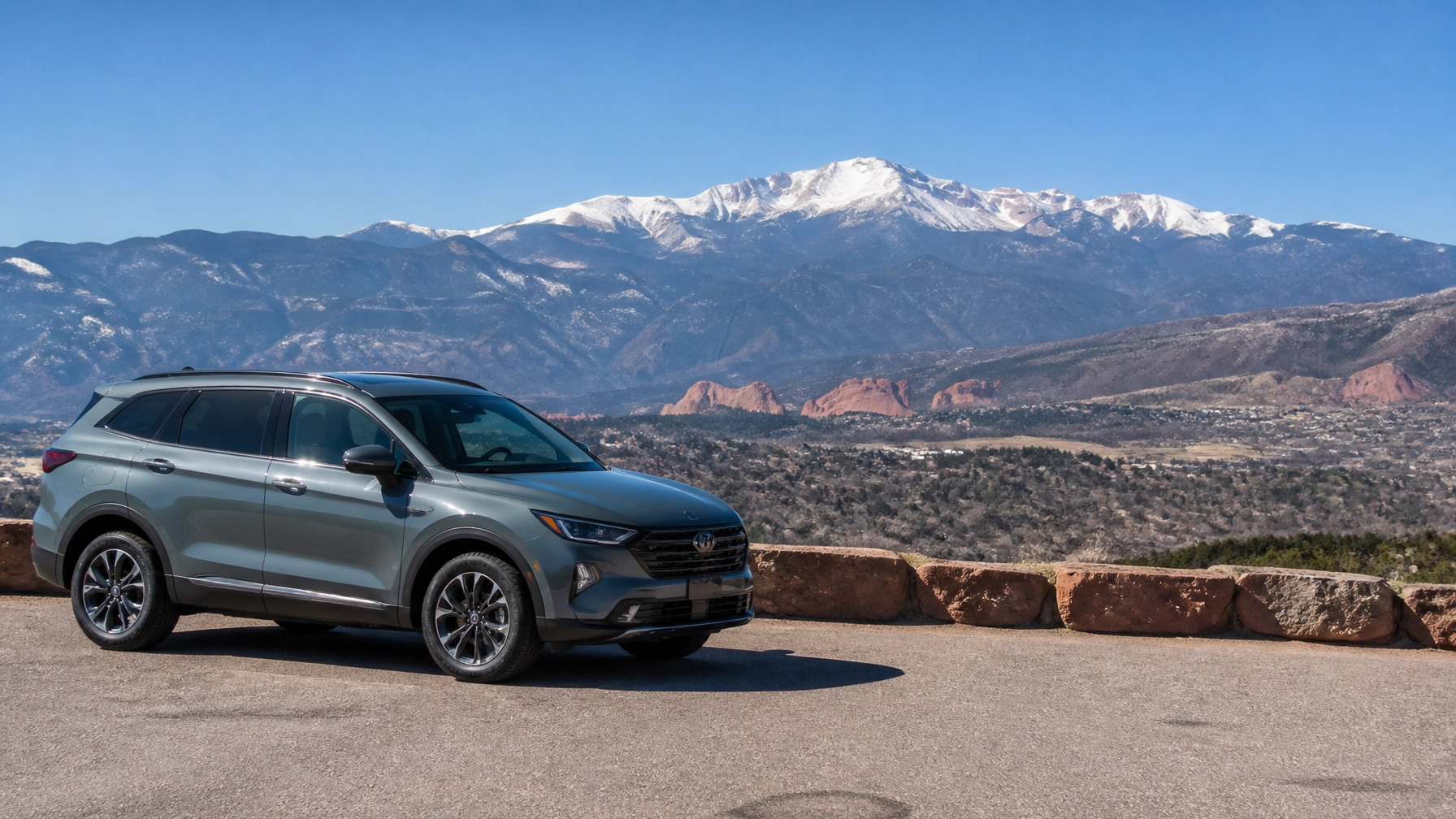 A modern hybrid SUV parked on a scenic overlook in Colorado Springs with a clear view of Pikes Peak in the background during a bright, sunny day