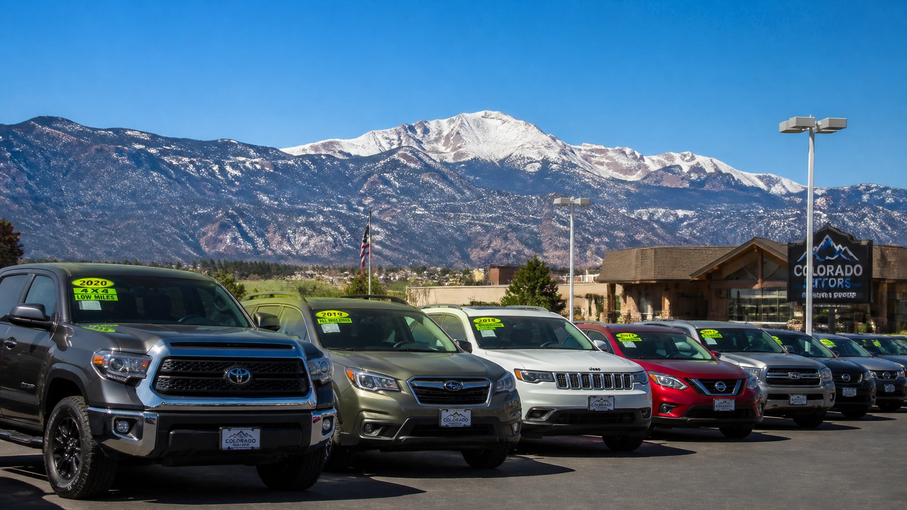 A diverse selection of pre-owned vehicles on a clean Colorado Springs car lot with Pikes Peak in the background