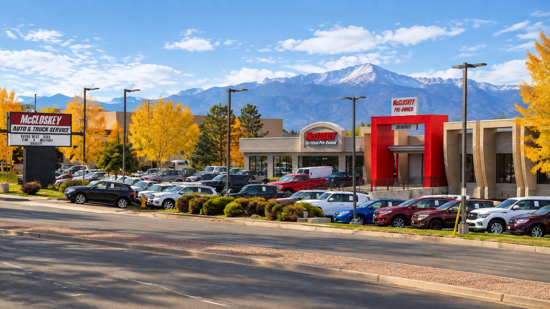 McCloskey Motors used vehicle lot in Colorado Springs during autumn with golden trees and Pikes Peak in the background