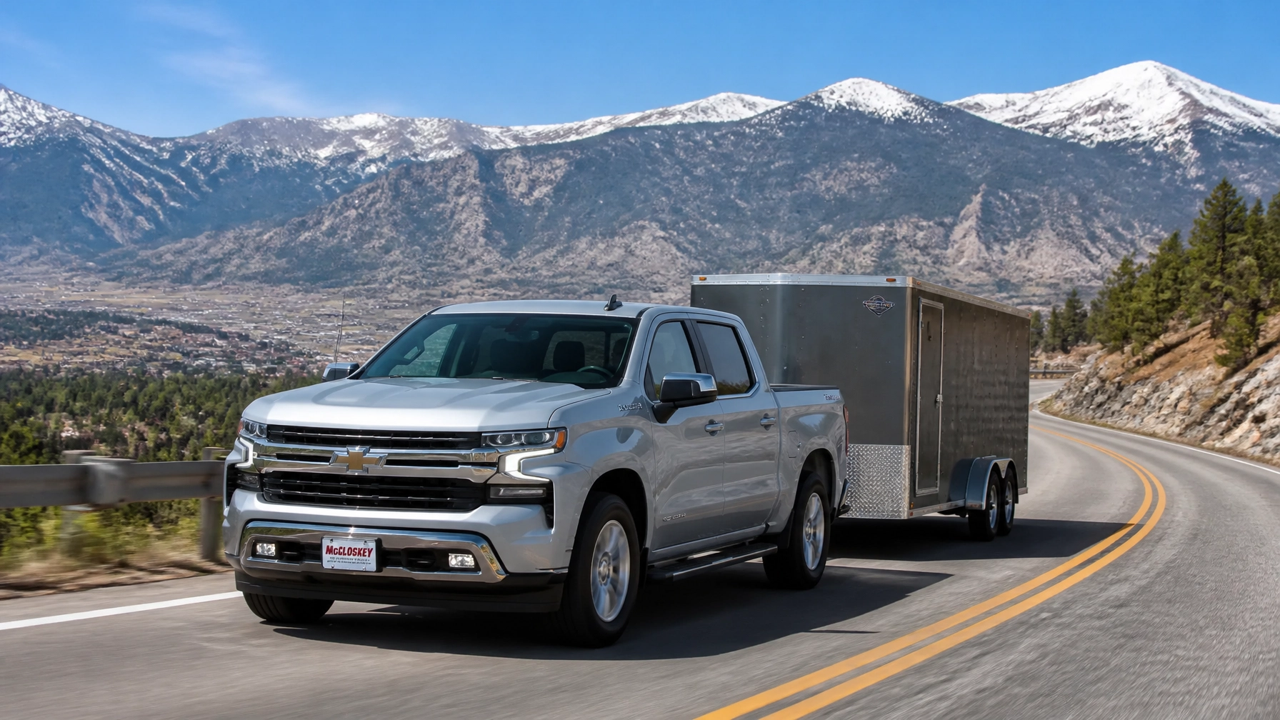 Silver Chevrolet Silverado towing a trailer on a mountain road near Colorado Springs CO