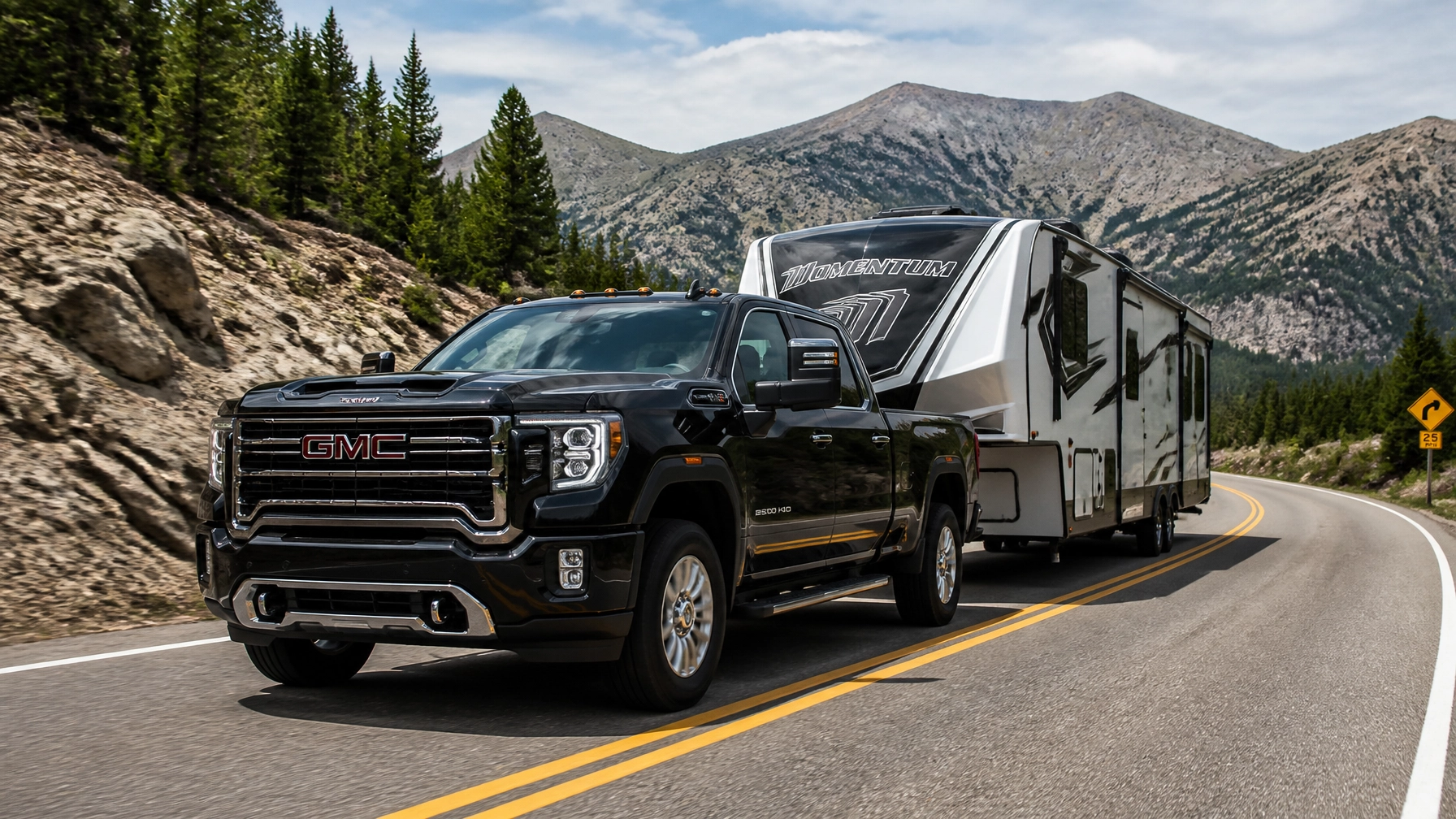 Late-model black GMC Sierra 2500 heavy-duty truck towing a large camping trailer on a mountain road in Colorado