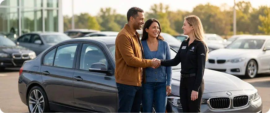 Salesperson shaking hands with a happy customer beside a BMW at the dealership