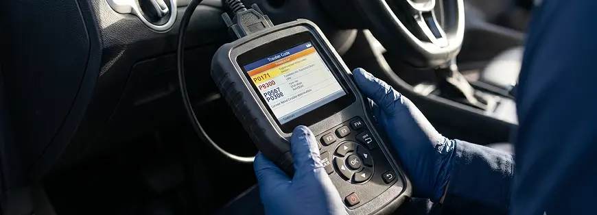 Gloved technician holding an OBD-II scan tool displaying trouble codes inside a vehicle