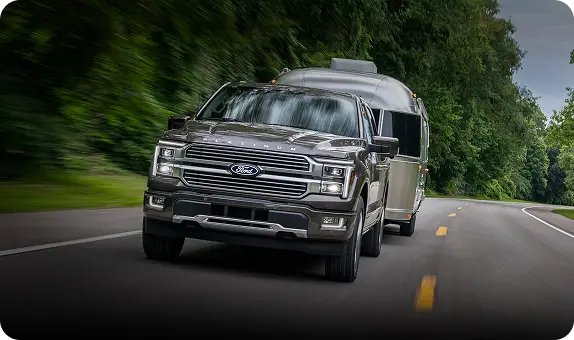 Gray Ford F-150 PowerBoost hybrid towing a trailer on a tree-lined highway