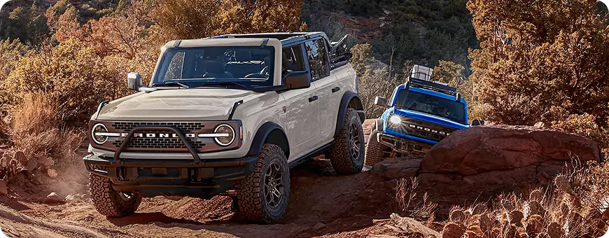 Two Ford Broncos climbing a rocky red-rock trail
