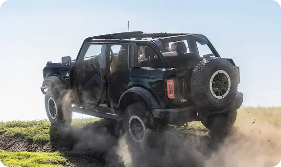 Open-top Ford Bronco driving off-road on a dusty trail