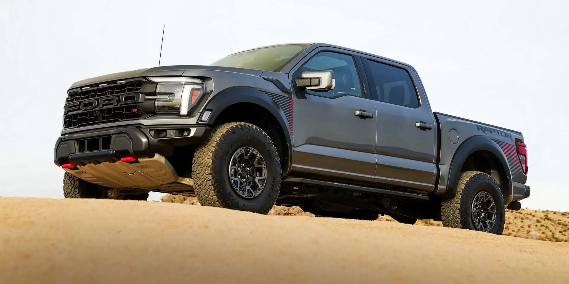 Gray Ford F-150 Raptor front three-quarter view on desert terrain