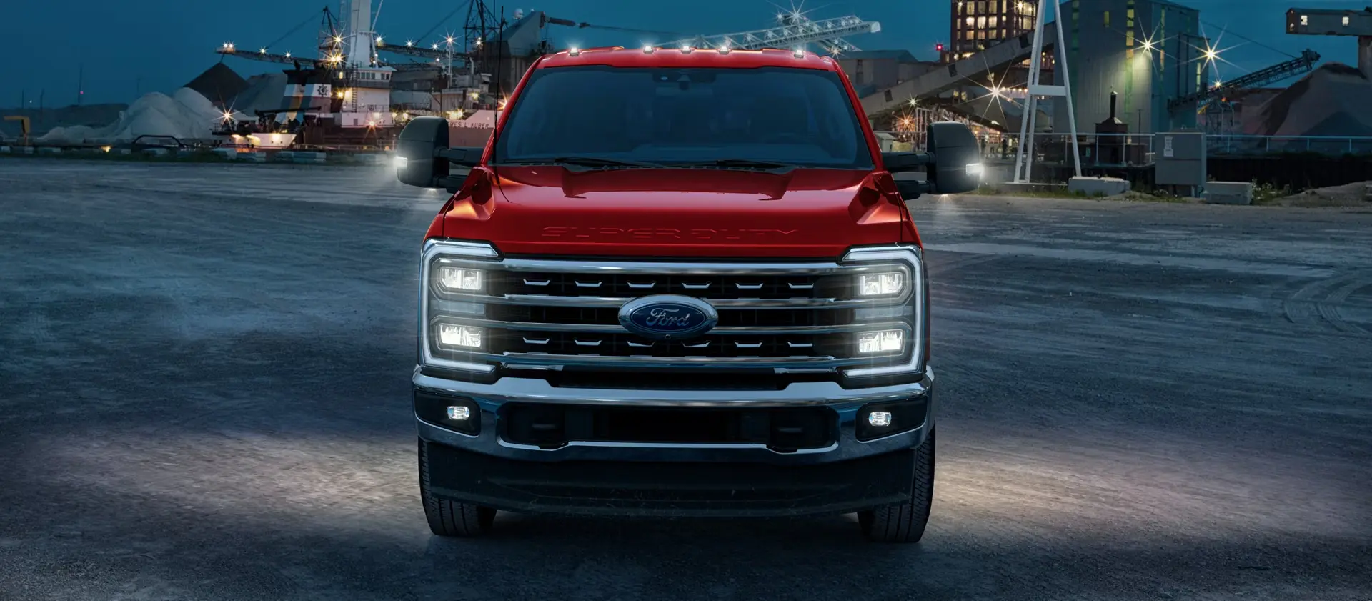 Red Ford Super Duty front view at an industrial worksite at dusk