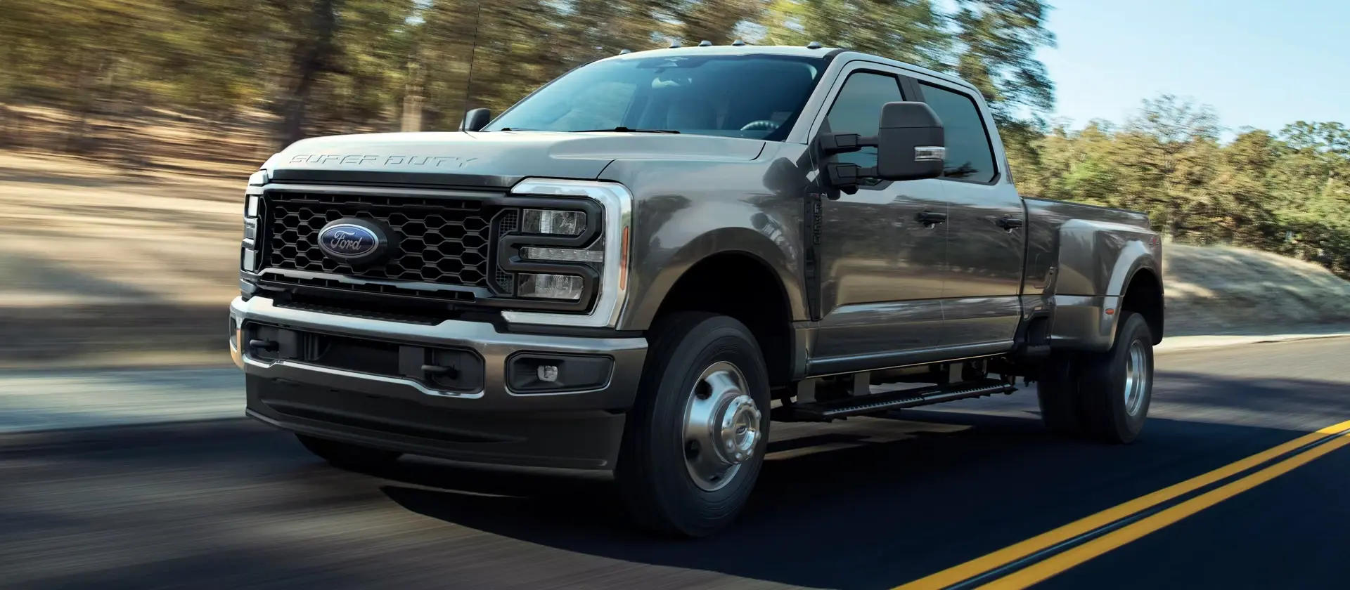 Tan Ford Super Duty dually driving on the road, front three-quarter view