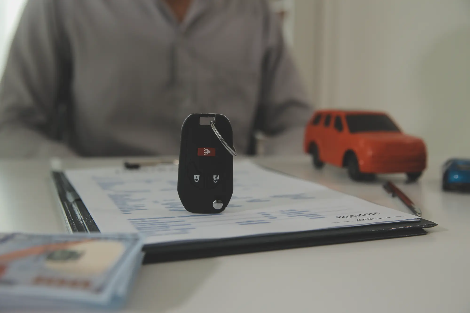 Car key on a signed auto loan agreement with a salesperson in the background
