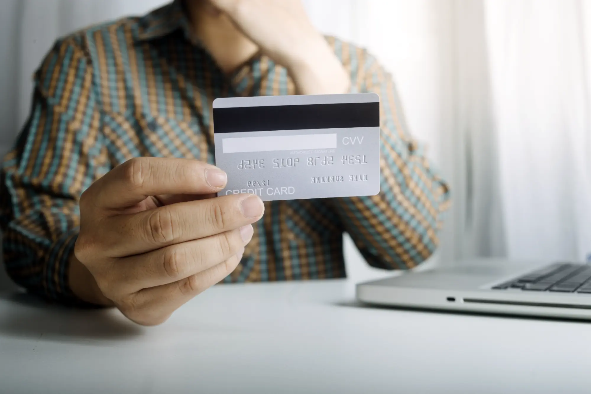 Man holding a credit card next to a laptop while checking his auto loan credit score online.