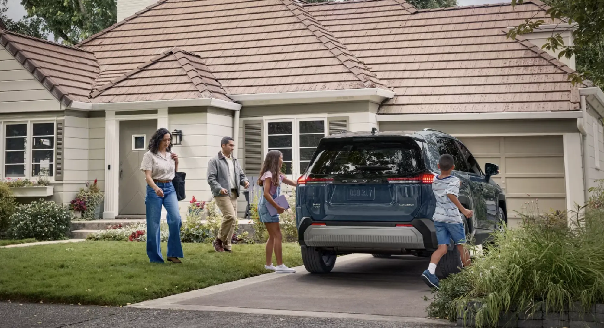 Family of four loading into a blue Toyota RAV4 Limited Hybrid AWD parked in the driveway of their home