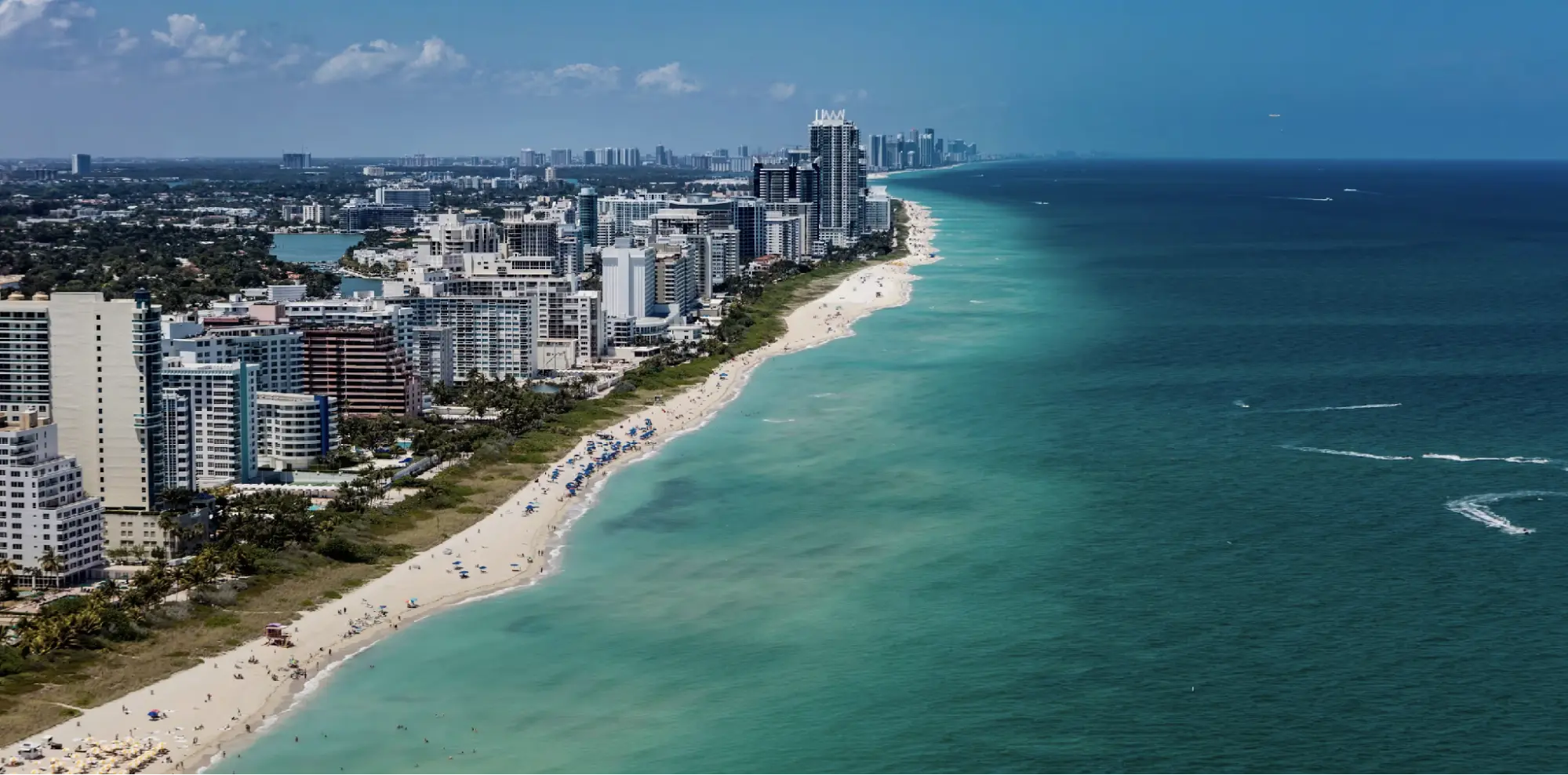 Aerial view of a Florida coastline with high-rise buildings lining a sandy beach next to turquoise ocean water