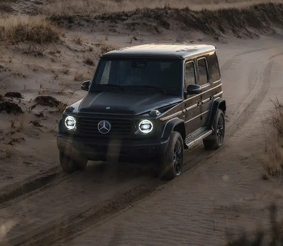 Black Mercedes-Benz G-Class driving on desert sand, front three-quarter view
