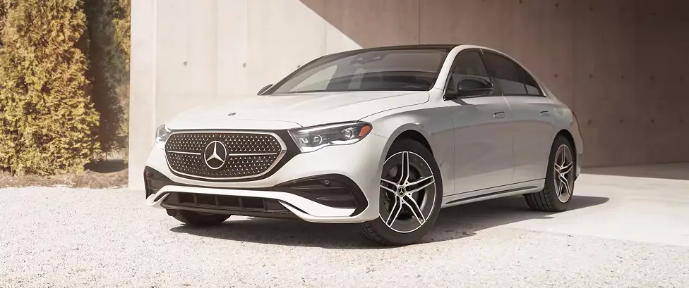 Silver Mercedes-Benz E-Class sedan parked by a concrete wall, front three-quarter view