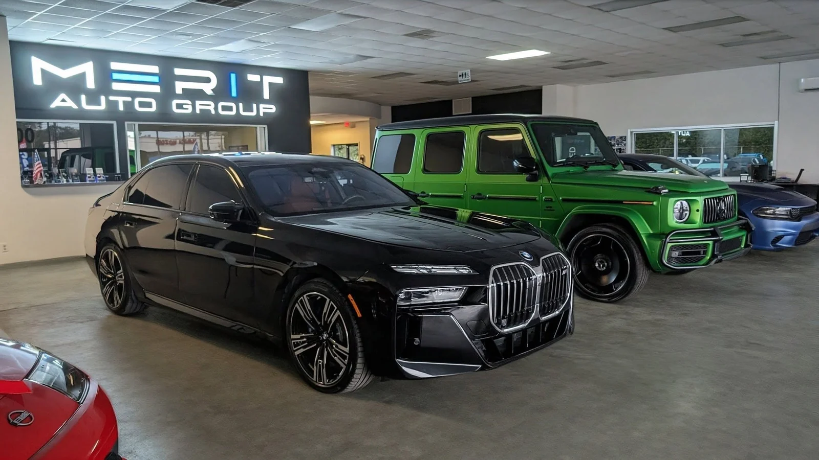 Merit Auto Group showroom in Jacksonville, FL with a BMW 7 Series, a Mercedes-Benz G-Class, and a Dodge Charger on the floor