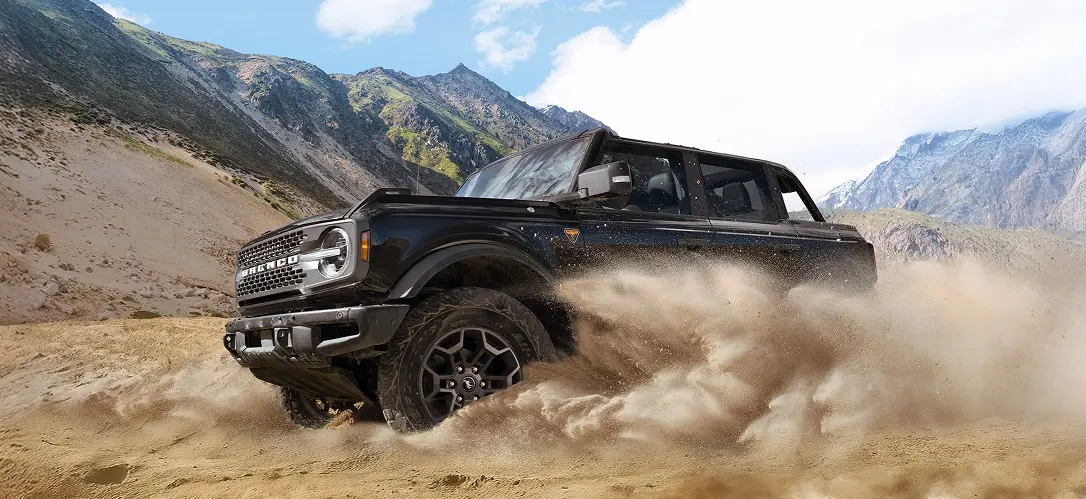 Black Ford Bronco driving off-road through sand and dirt