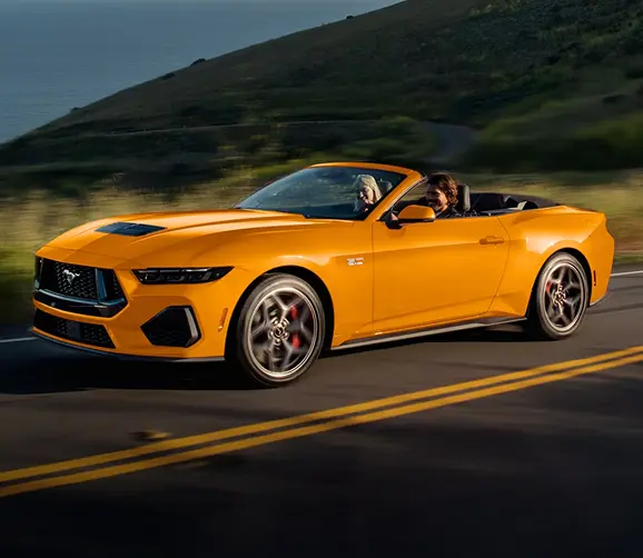 Orange Ford Mustang GT convertible driving on a coastal road