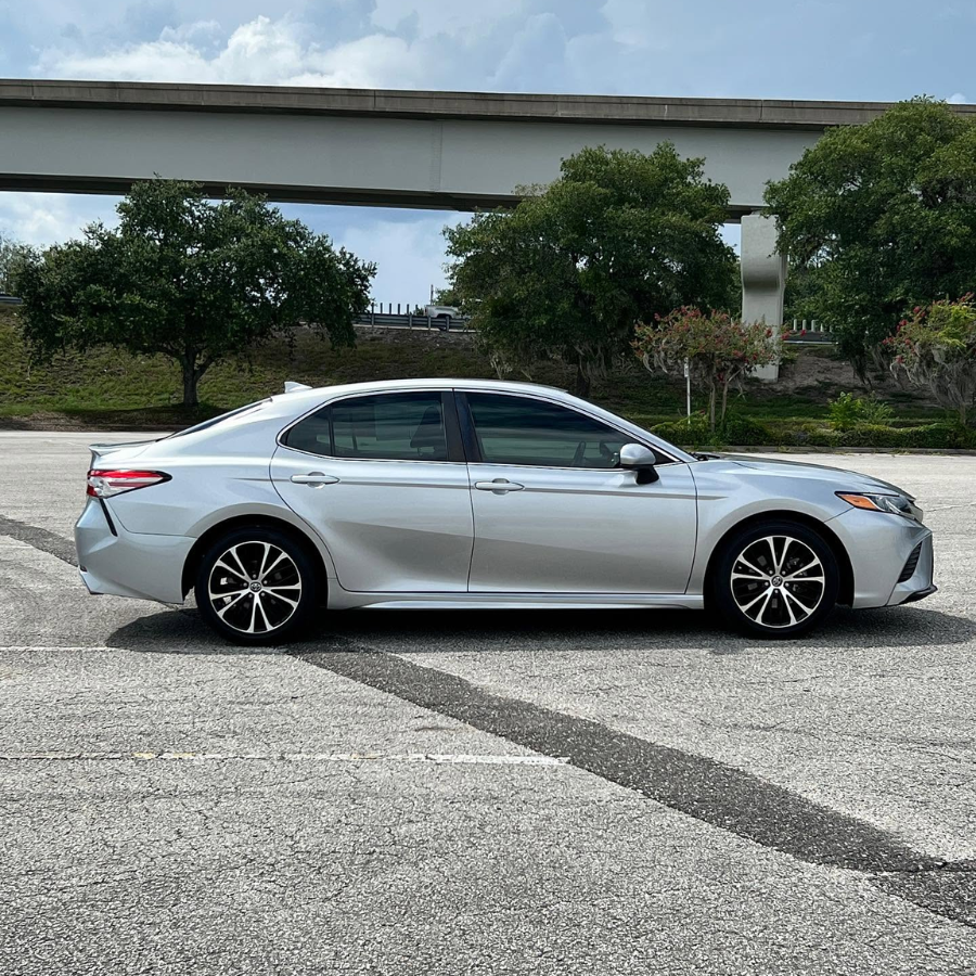 Silver Toyota Camry in full side profile, parked under an overpass.