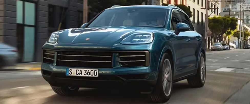 Teal Porsche Cayenne driving through a city street