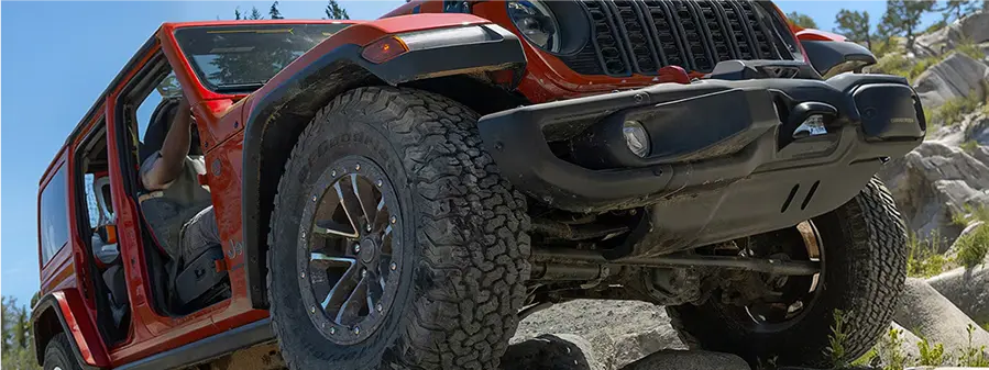 Front of a red Jeep Wrangler showing its approach angle on rocks