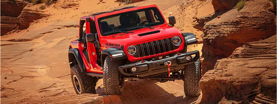 Red Jeep Wrangler driving over desert rocks