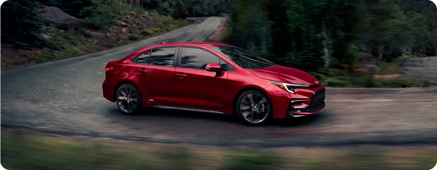 Red Toyota Corolla driving on a city street, front three-quarter view