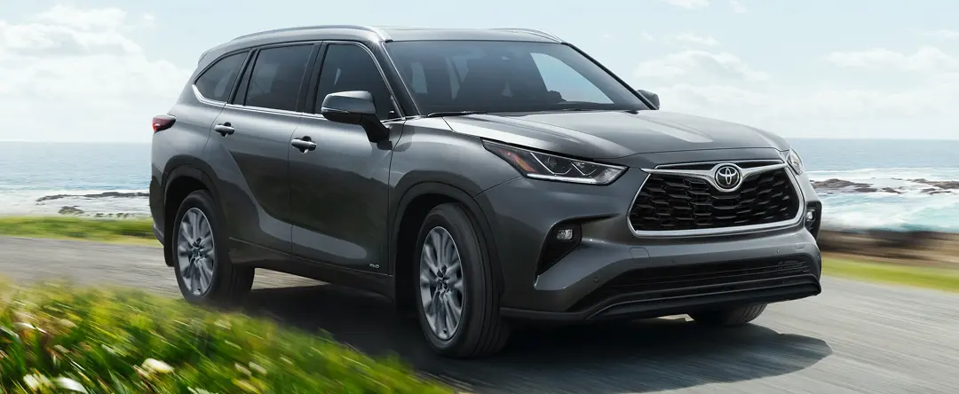 Gray Toyota Highlander driving along a coastal road, front three-quarter view