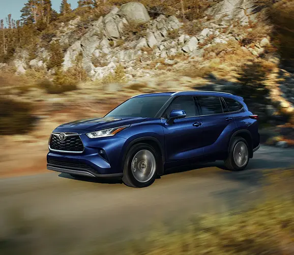Blue Toyota Highlander driving on a coastal road, front three-quarter view