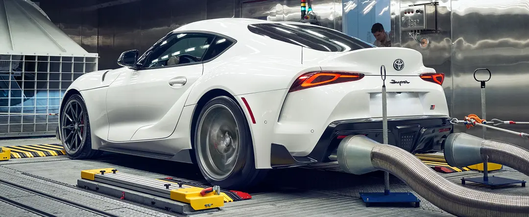 White Toyota GR Supra on a dynamometer in a workshop, rear three-quarter view