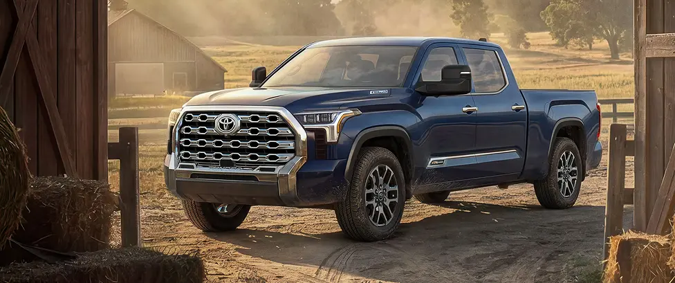 Blue Toyota Tundra i-FORCE MAX pickup parked by a barn at golden hour, front three-quarter view