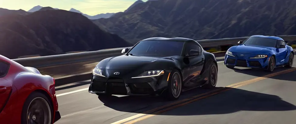 Red, black, and blue Toyota GR Supra coupes driving together on a mountain road