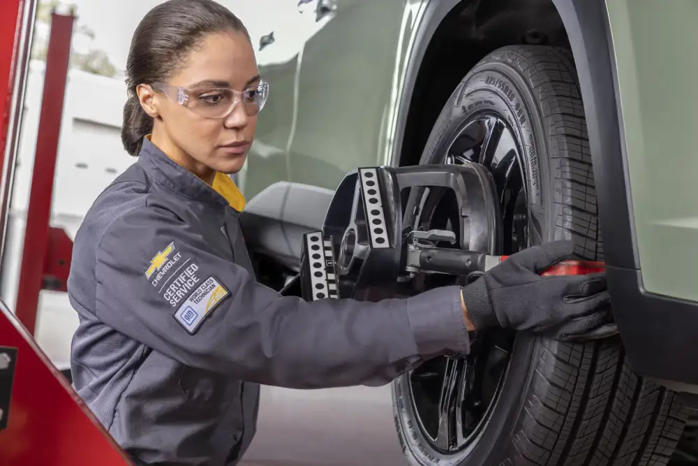 Technician wearing safety glasses installing a brake component on a vehicle's wheel in a service bay.