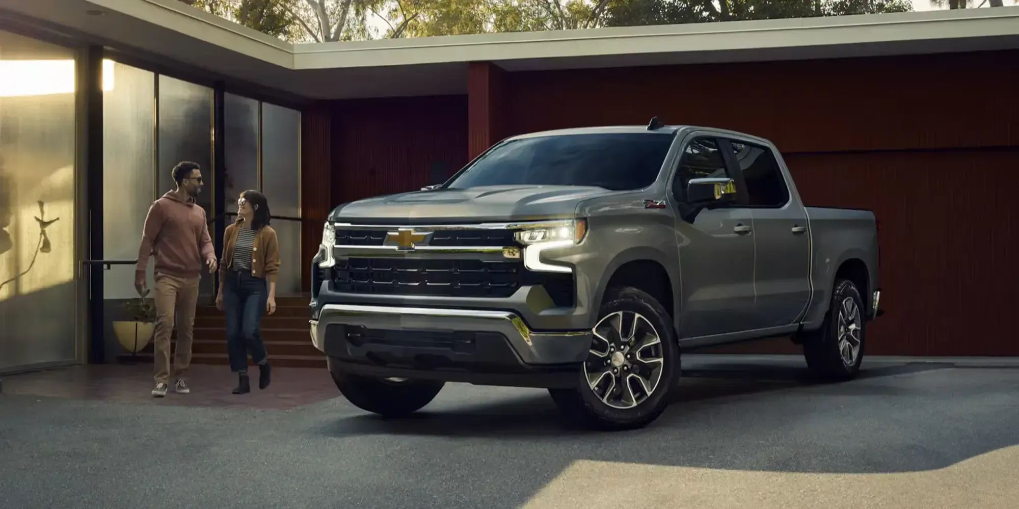Couple walking toward a gray Chevrolet Silverado crew cab parked in the driveway of a modern home.