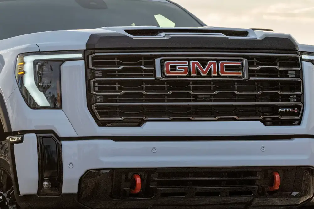 Close-up front view of a white GMC AT4 truck showing its grille, headlights, and front bumper.
